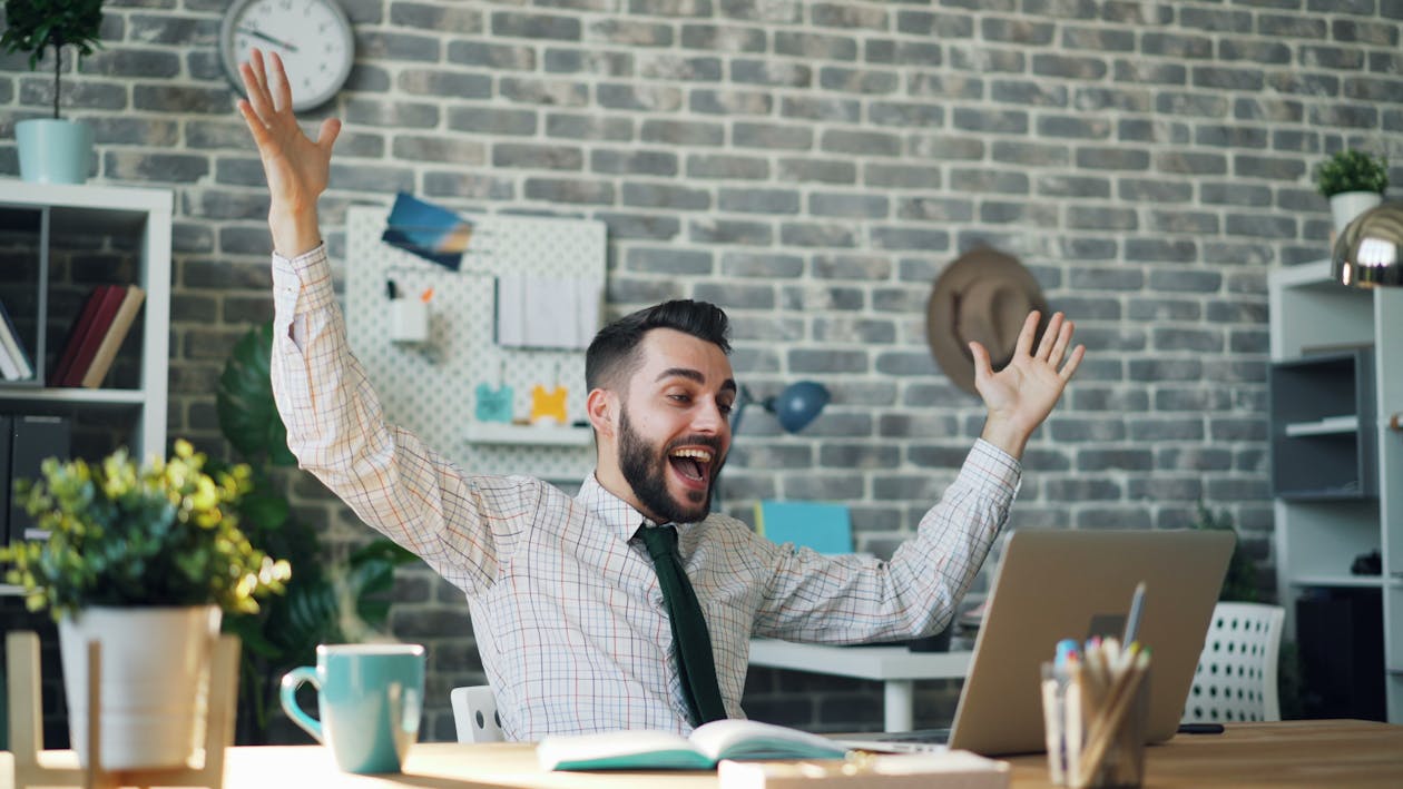 Office worker celebrating success at laptop - representing the joy of achieving the biggest company sale
